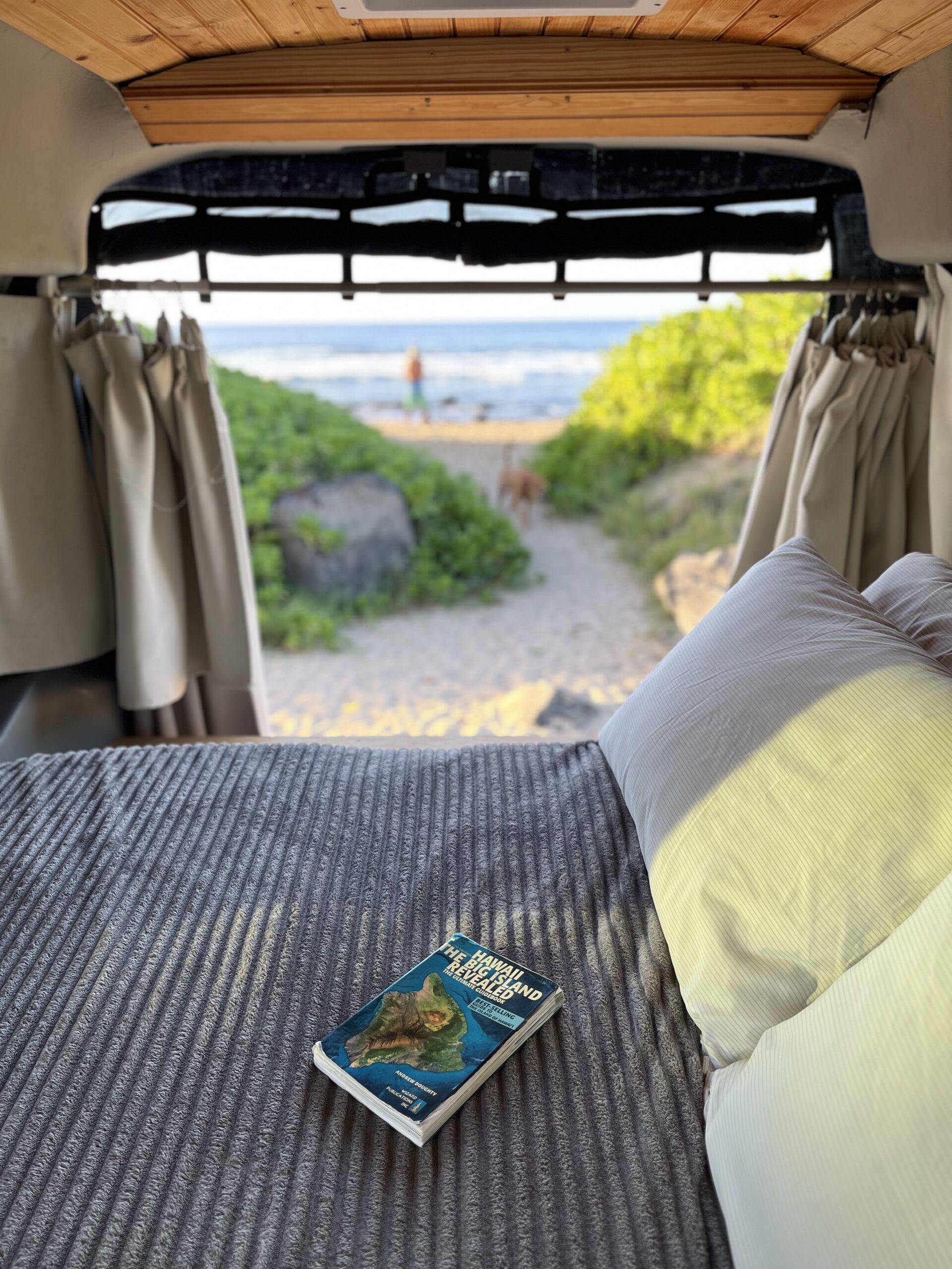 Kona camper van parked next to the ocean with Big Island Revealed Book on the bed