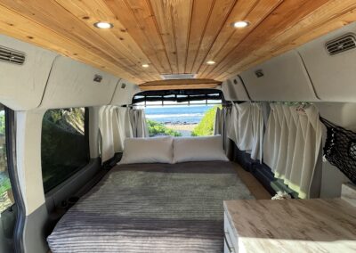 Long bed setup inside Carlos camper van with soft lighting and organized storage